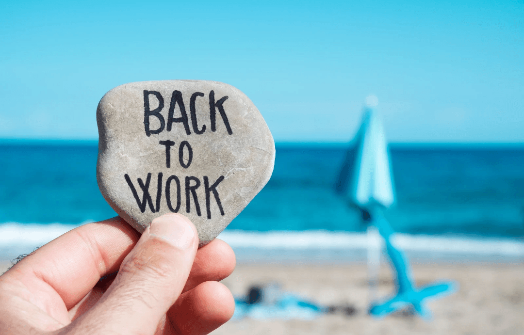 Galet avec l'inscription « Back to work » tenu face à la mer, symbole de la rentrée après les vacances